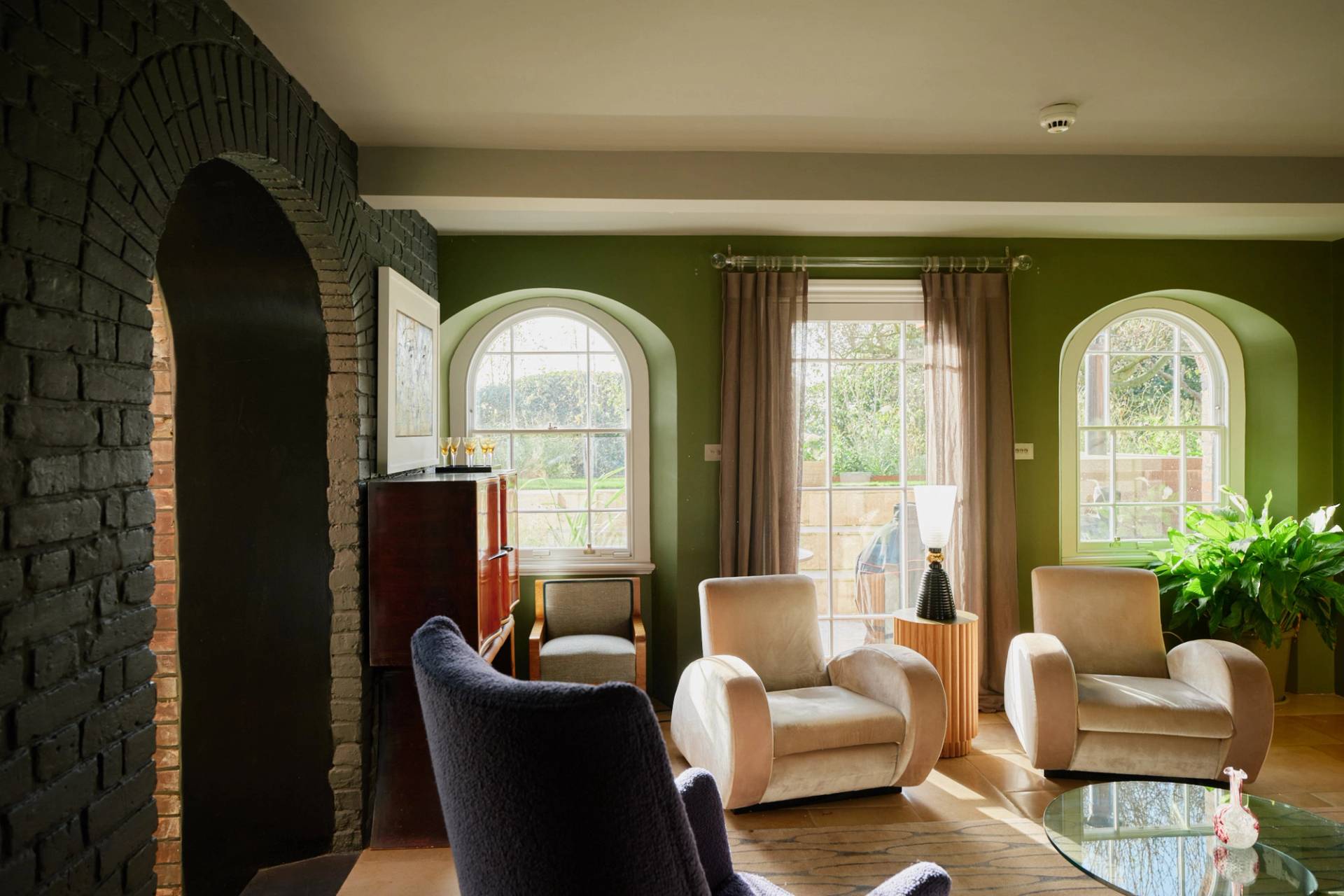 Sage green living room featuring twin velvet armchairs, arched sash windows, and light wood floorboards, ideal for furniture lookbooks, Love Locations SW20.