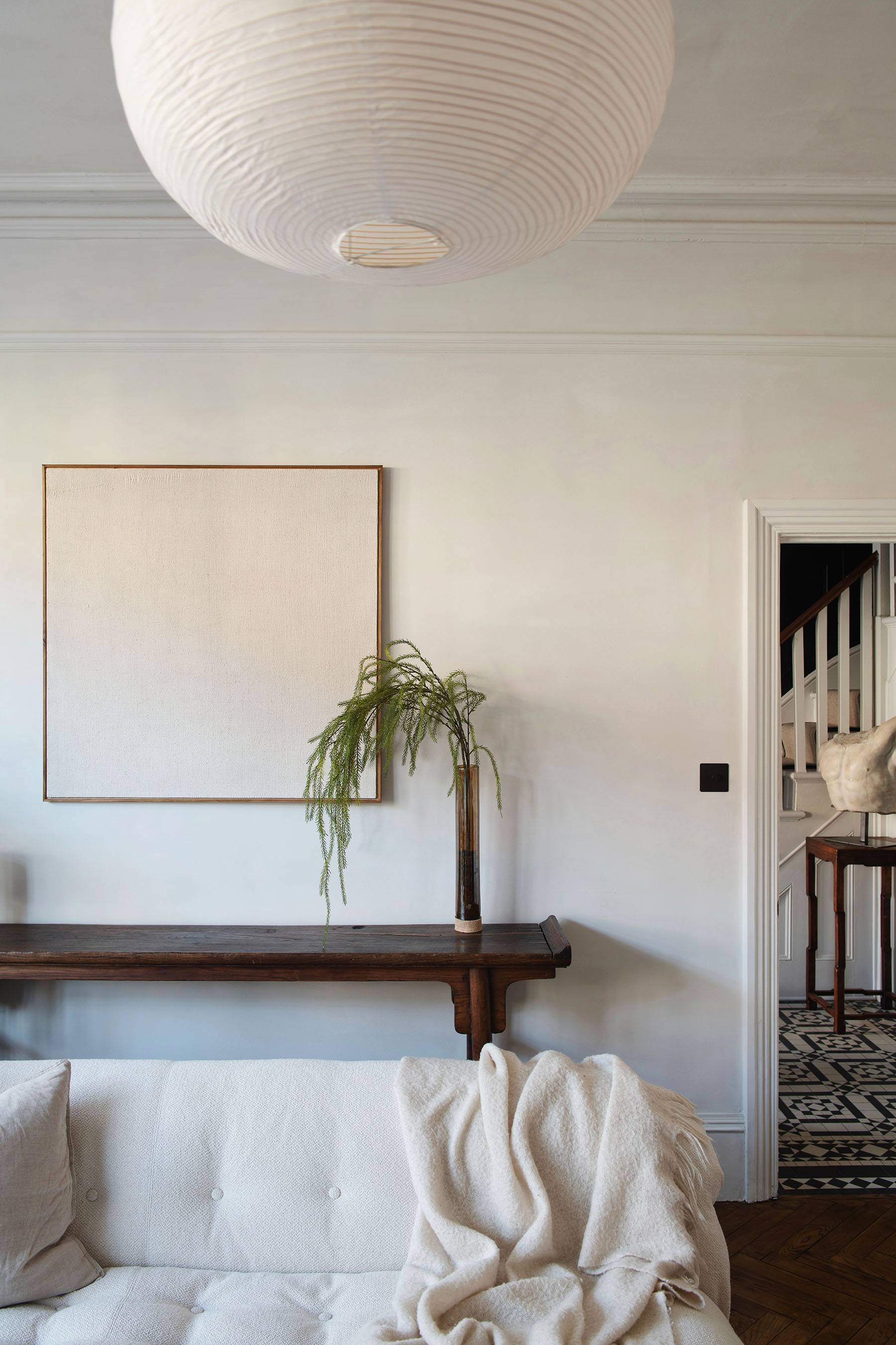 Wabi-sabi lounge detail with raw plaster wall backdrop, dark wood armchair, and stacked firewood alcove, Love Locations SW16.