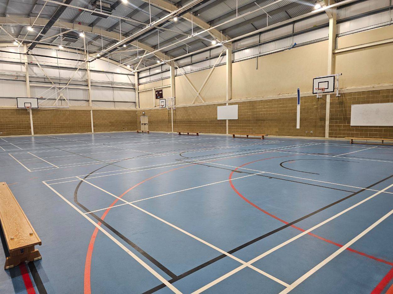 Huge school gymnasium filming location featuring a modern blue court surface and high-intensity industrial lighting, Love Locations HP13.
