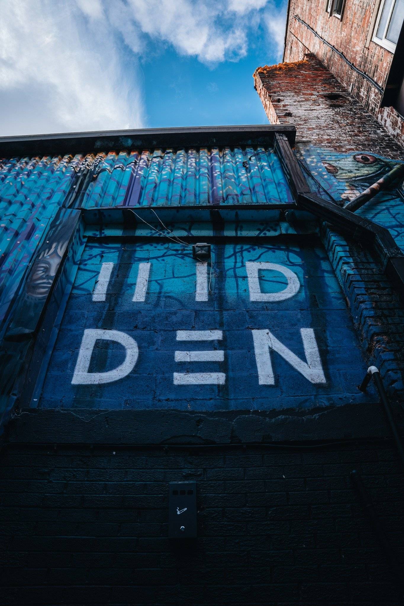 Branded blue corrugated metal wall entrance with HIDDEN signage at a Cheetham Hill venue through Love Locations.
