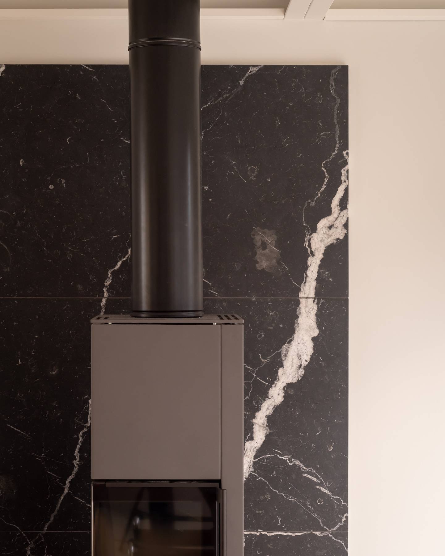Close-up detail of a black wood-burning stove set against a white veined black marble hearth wall, Love Locations BN3.