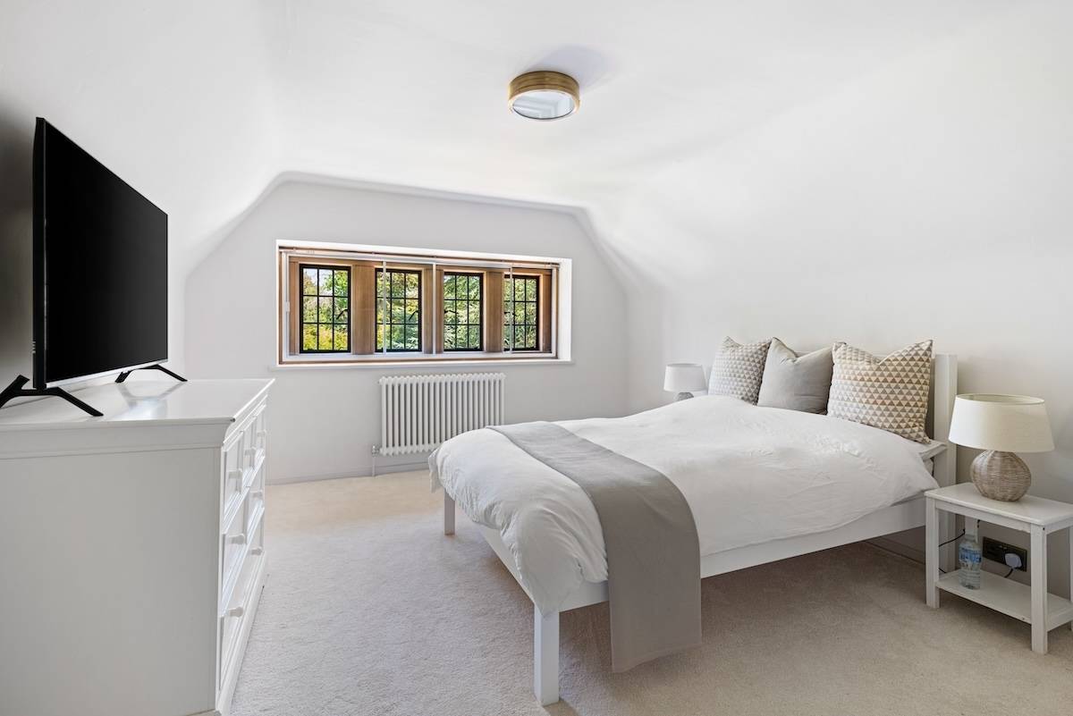 Attic bedroom with sloped ceilings, white furniture, and a leaded window overlooking grounds, Love Locations RH13.