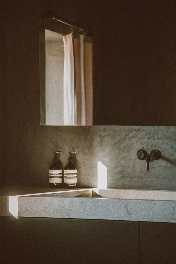 Minimalist stone sink vanity with wall-mounted black taps set under warm sunlight, Love Locations 07630.