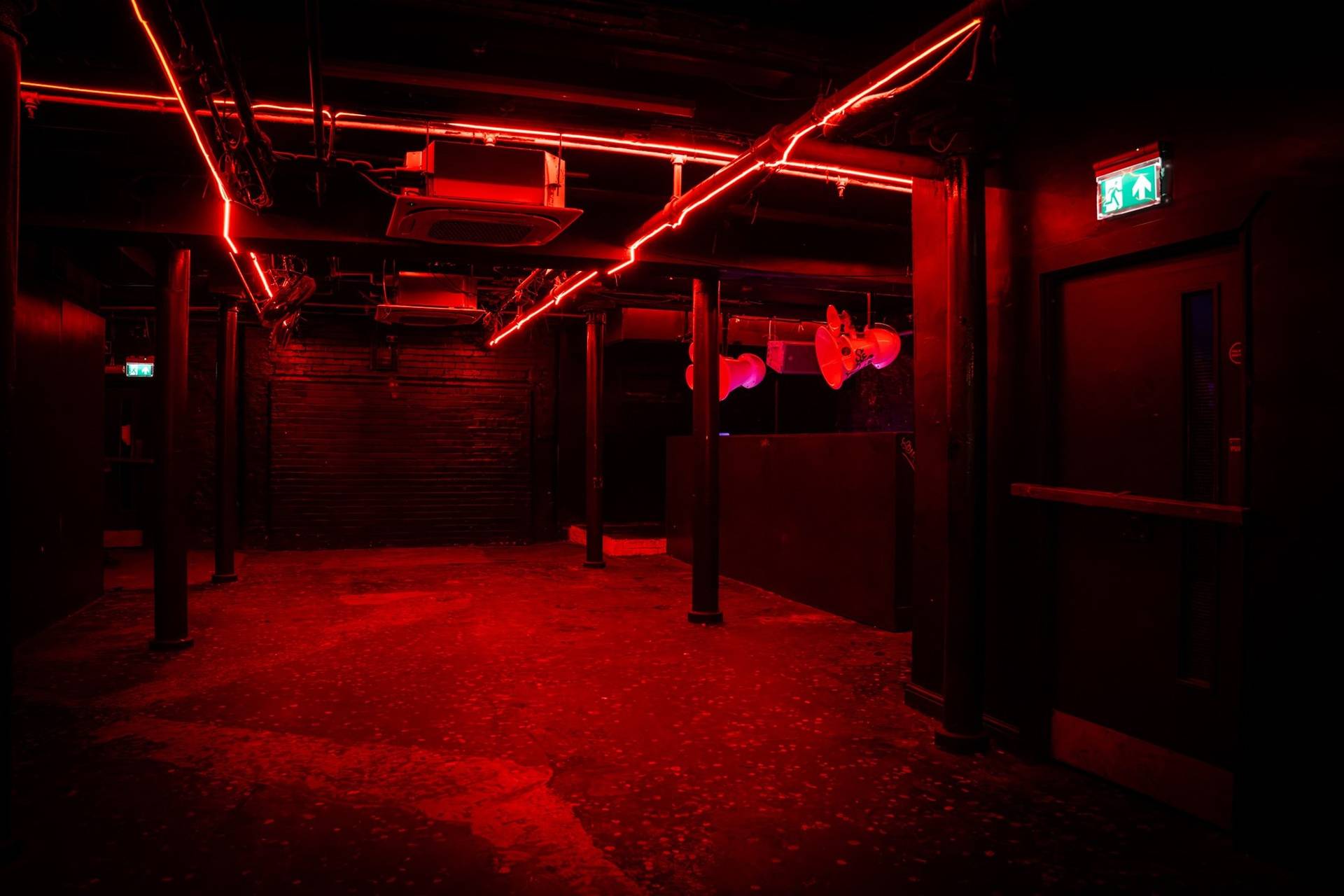 Red-lit industrial club space featuring overhead cable trays and dark brick walls in Manchester M3 by Love Locations.