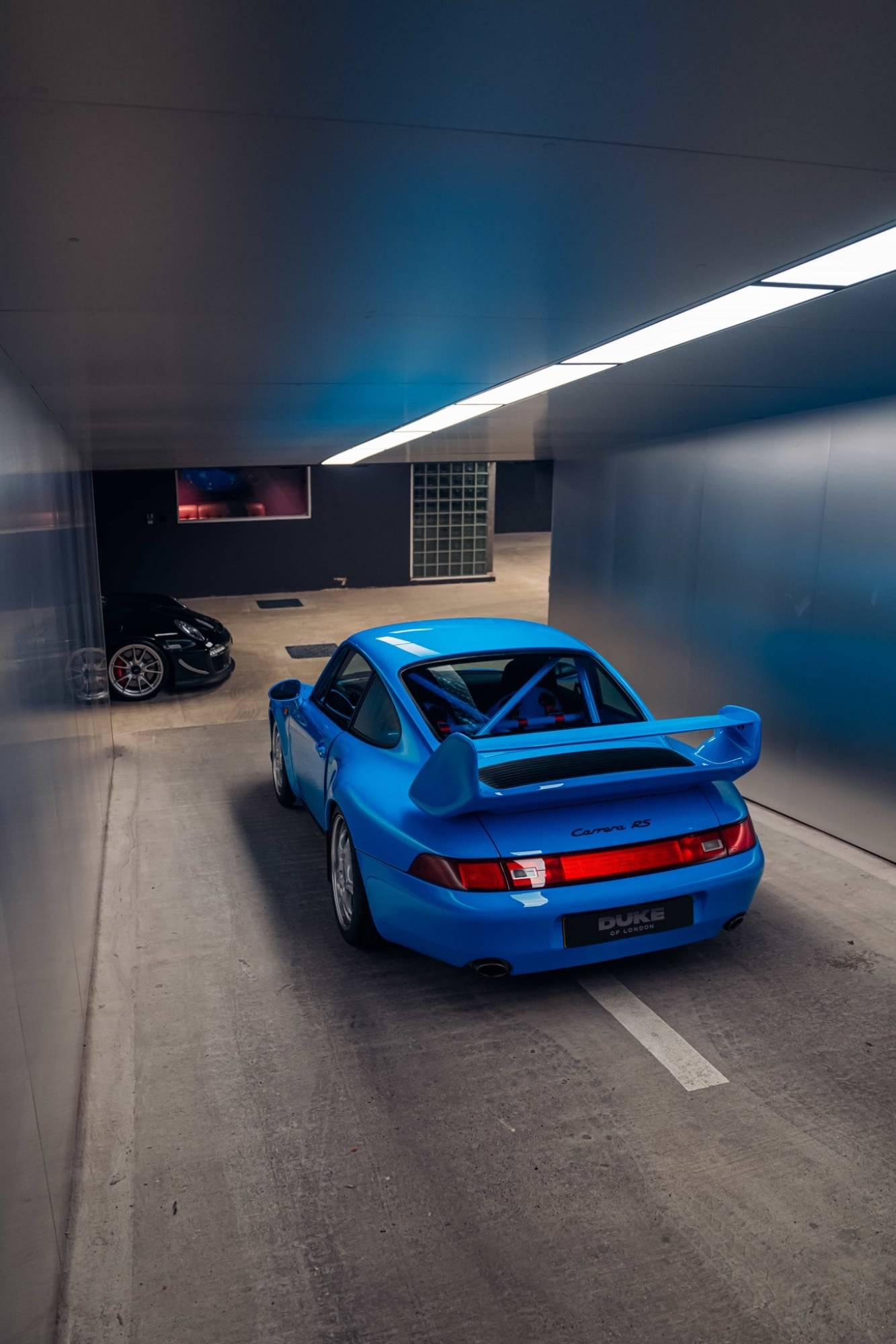 Rear angle view of a blue Porsche Carrera RS in a subterranean concrete garage shoot space through Love Locations.