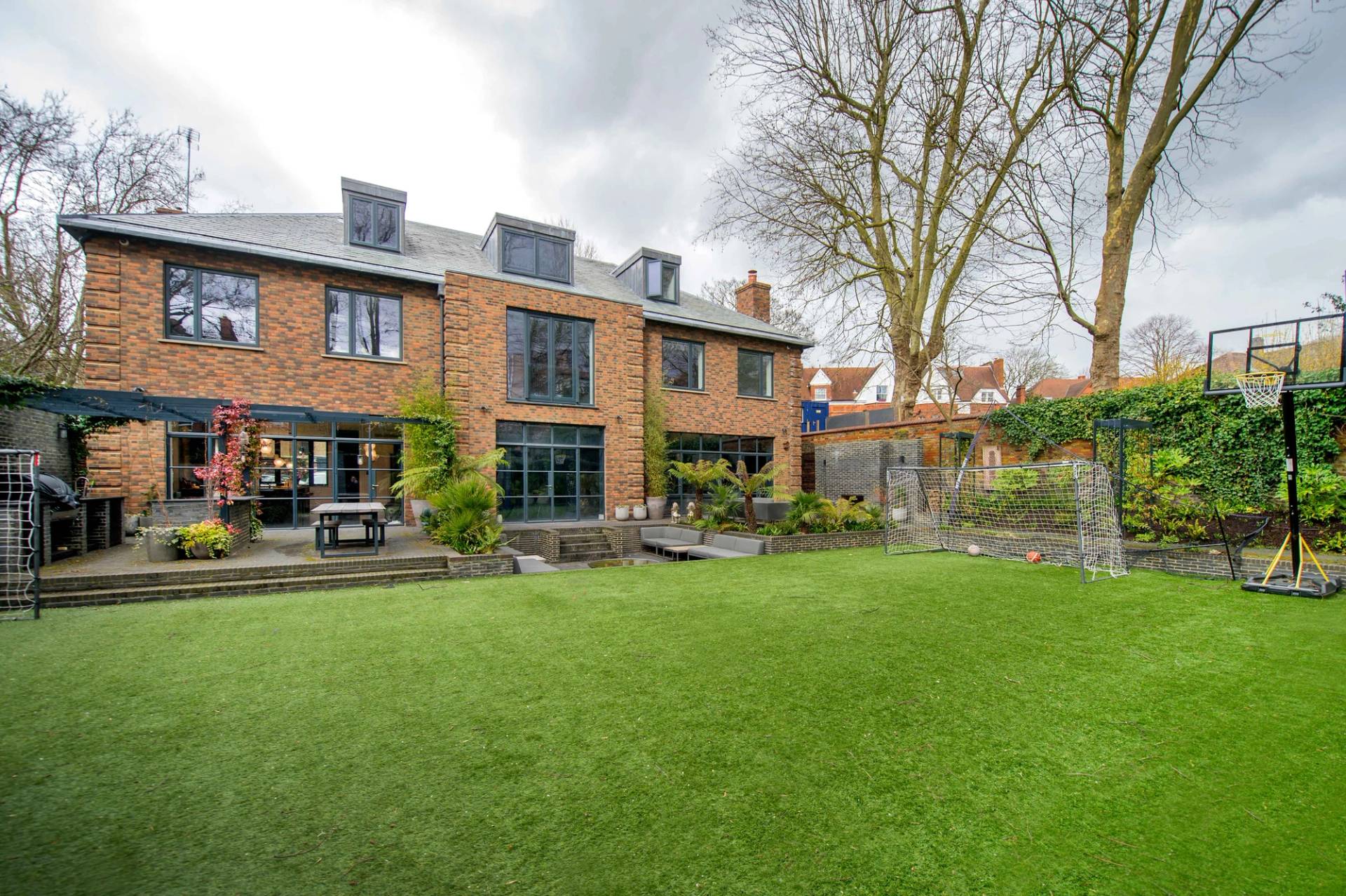 Rear exterior facade of a luxury red brick townhouse property in Belsize Park, NW3 featuring large Crittall-style windows and a pristine lawn, Love Locations.