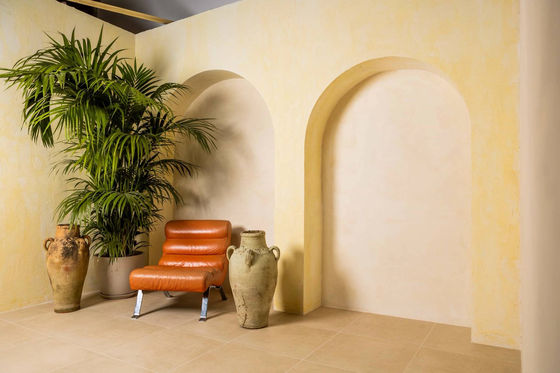 Creative photography studio set in Tottenham, N15 featuring plaster Mediterranean wall arches, terracotta leather lounge chair, and stone amphora urn via Love Locations.