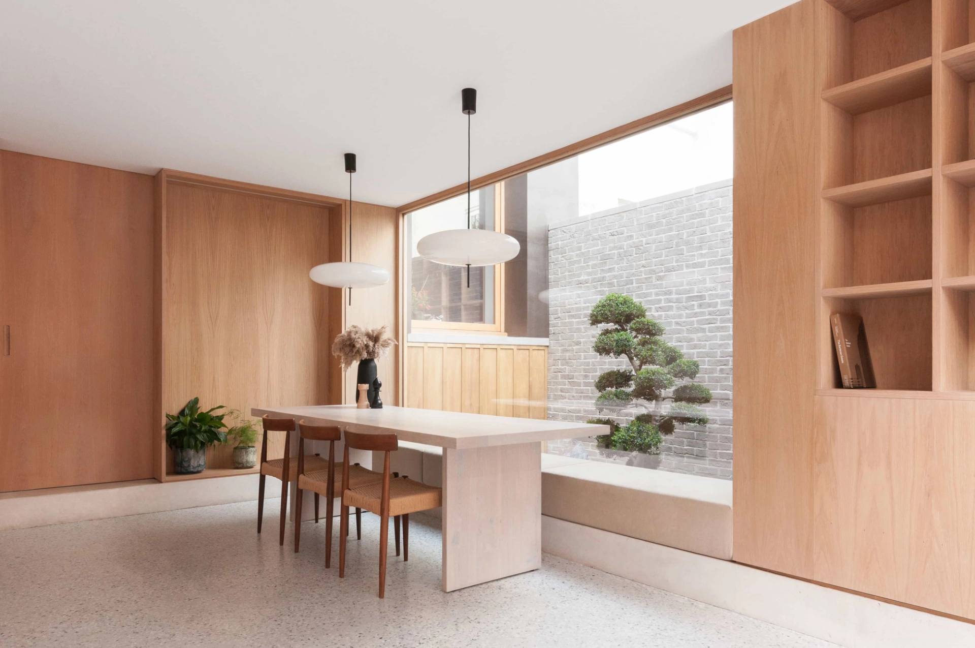Minimalist open-plan light oak dining room shoot location in Hackney London N16 from Love Locations, featuring custom wood wall paneling, built-in bench seating, and a view into a sunken garden courtyard.