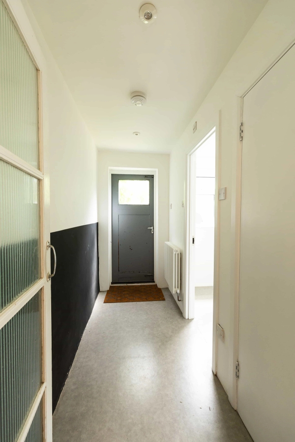 Love Locations minimalist hallway location E7: Clean white rear corridor with a black-framed privacy glass door leading out to the property's garden, configured for tracking video shots.