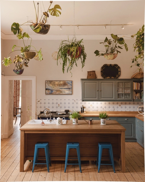 Spacious kitchen location featuring a central wooden island unit, hanging plants, and blue bar stools, Love Locations KY15.