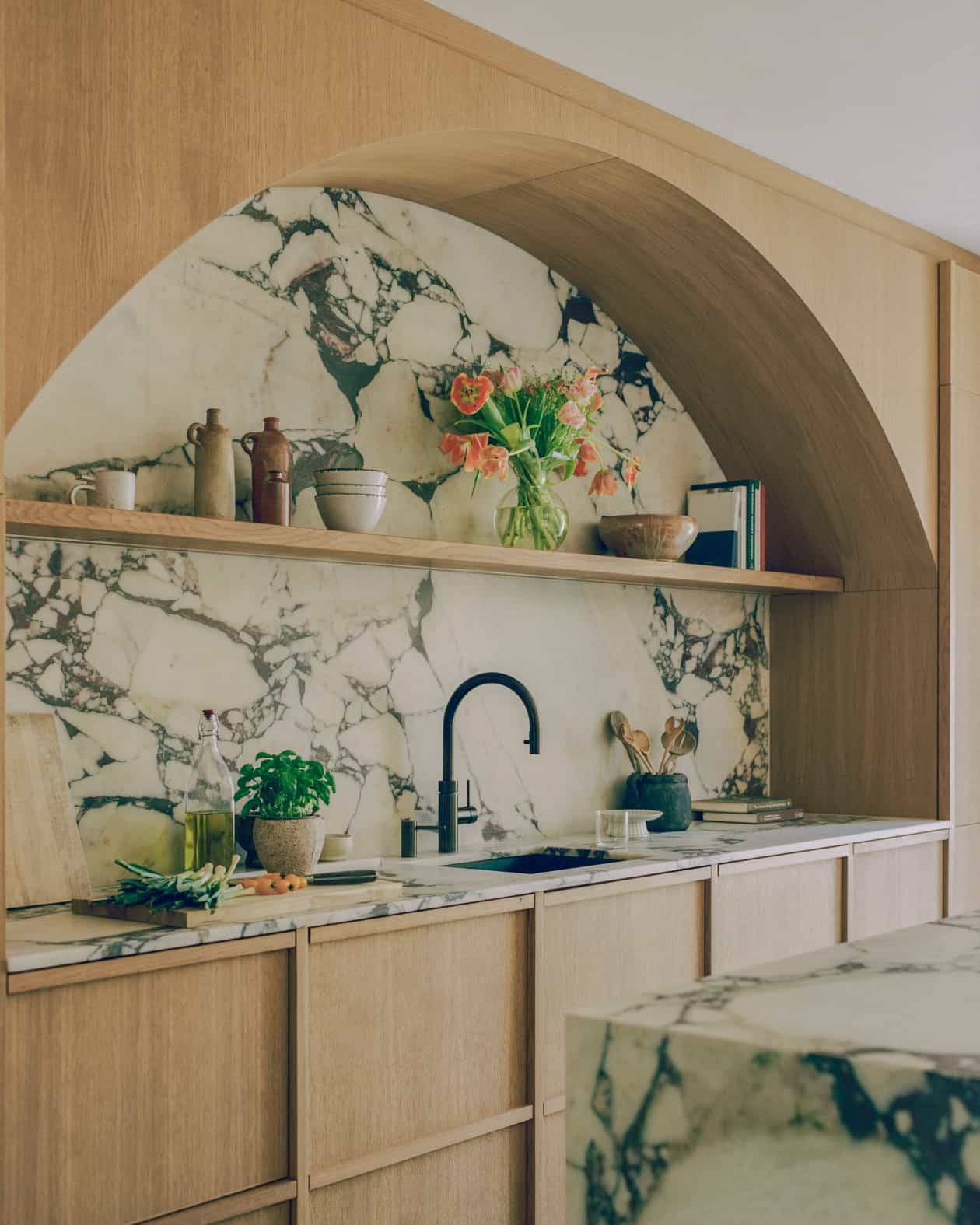 Close-up view of a green-veined marble kitchen backsplash set within a rounded oak arch alcove, Love Locations SW4.