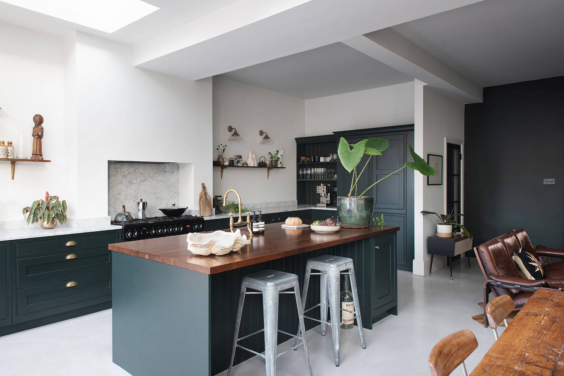 Wide-angle perspective of an industrial kitchen with dark green island, metal stools, skylights, and concrete floors, Love Locations.