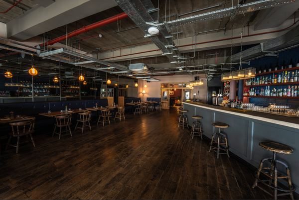 Wide-angle perspective of a large open-plan bar and event space with exposed ceiling ducts and industrial detailing, perfect for music video backdrops, Love Locations SW16.