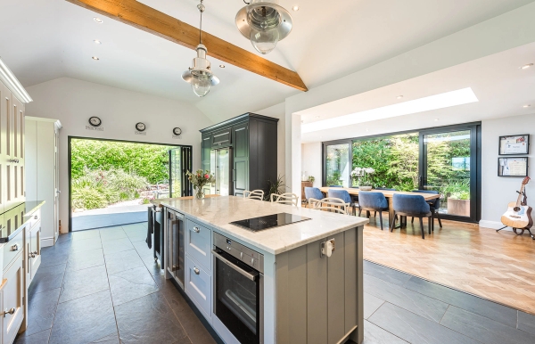Bright open-plan barn kitchen shoot space with bi-fold doors opening onto a scenic garden terrace, listed by Love Locations.
