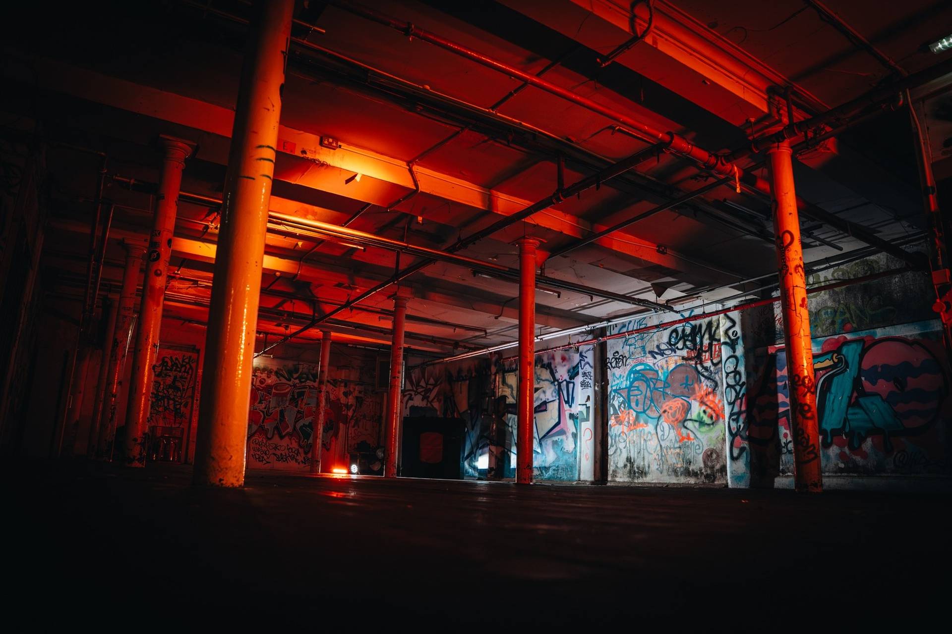 Gritty club location house for music video shoots in Cheetham Hill Manchester M3 via Love Locations, showcasing dark wooden floors, support columns, and vibrant red neon room lighting.