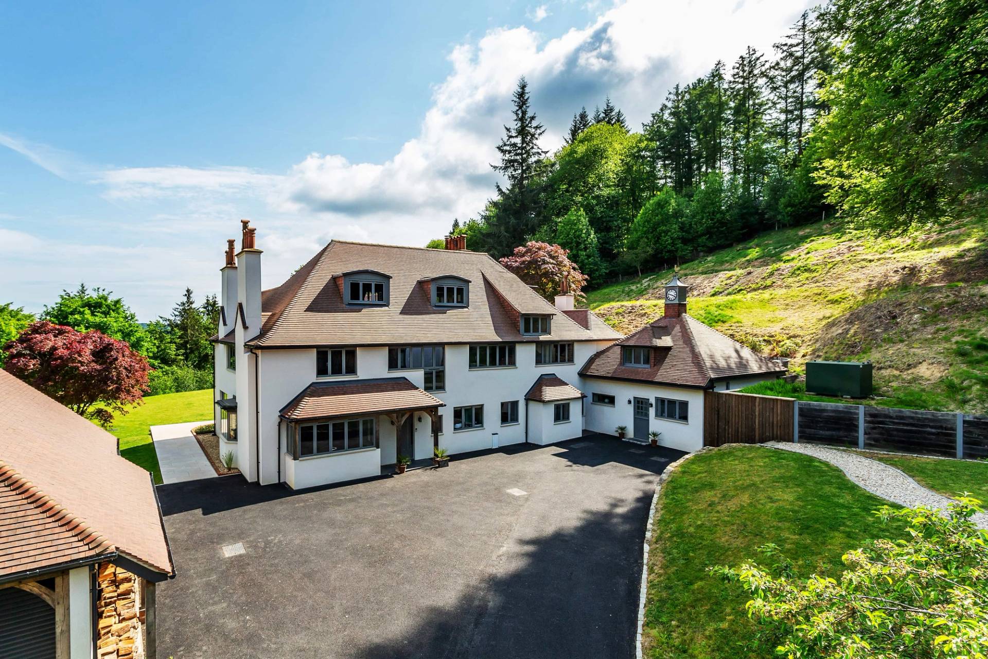 Rear facade shot of a white country house with traditional tiled roofs set into a lush green hillside in Surrey, Love Locations.