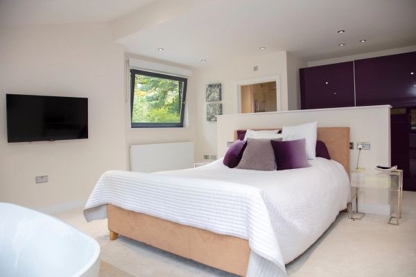 Luxury master bedroom location room with a freestanding oval bath, plush bedding, and a scenic garden window view, Love Locations.