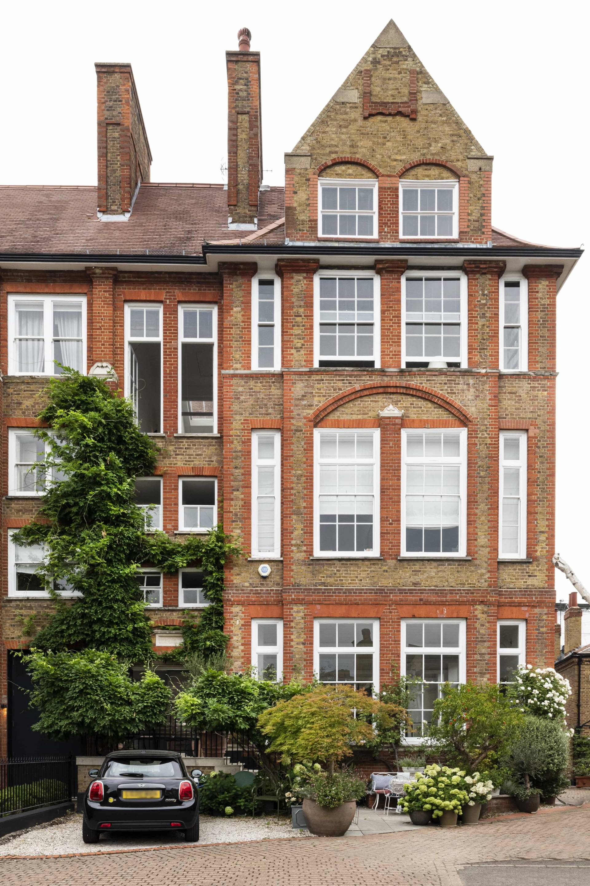 Converted Victorian schoolhouse shoot location hero cover image in Battersea, SW11 featuring a red brick facade, green ivy, multi-pane sash windows, Crittall glass partitions, and vaulted loft interiors, the ultimate high-visibility backdrop for fashion editorials, TV commercials, and commercial campaigns via Love Locations.
