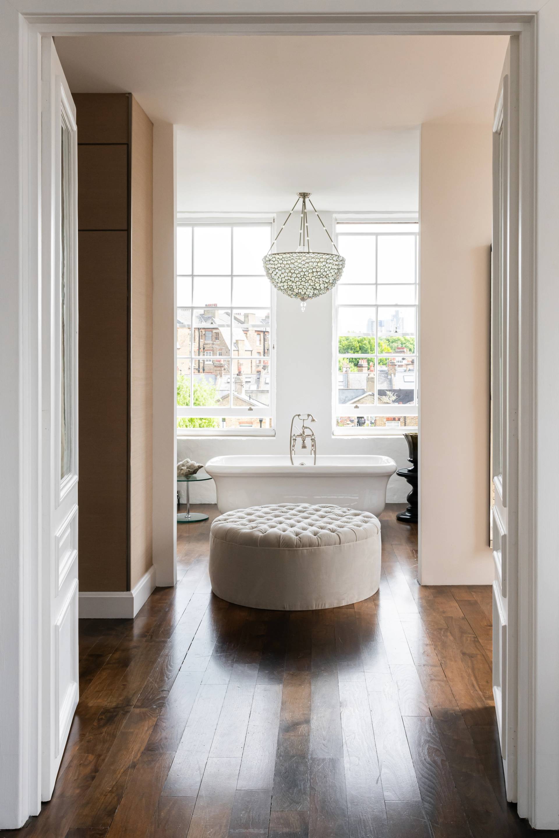 Luxury master bathroom suite featuring a freestanding soaking tub, round button-tufted ottoman, and large sash windows, ideal for skincare product marketing, Love Locations.