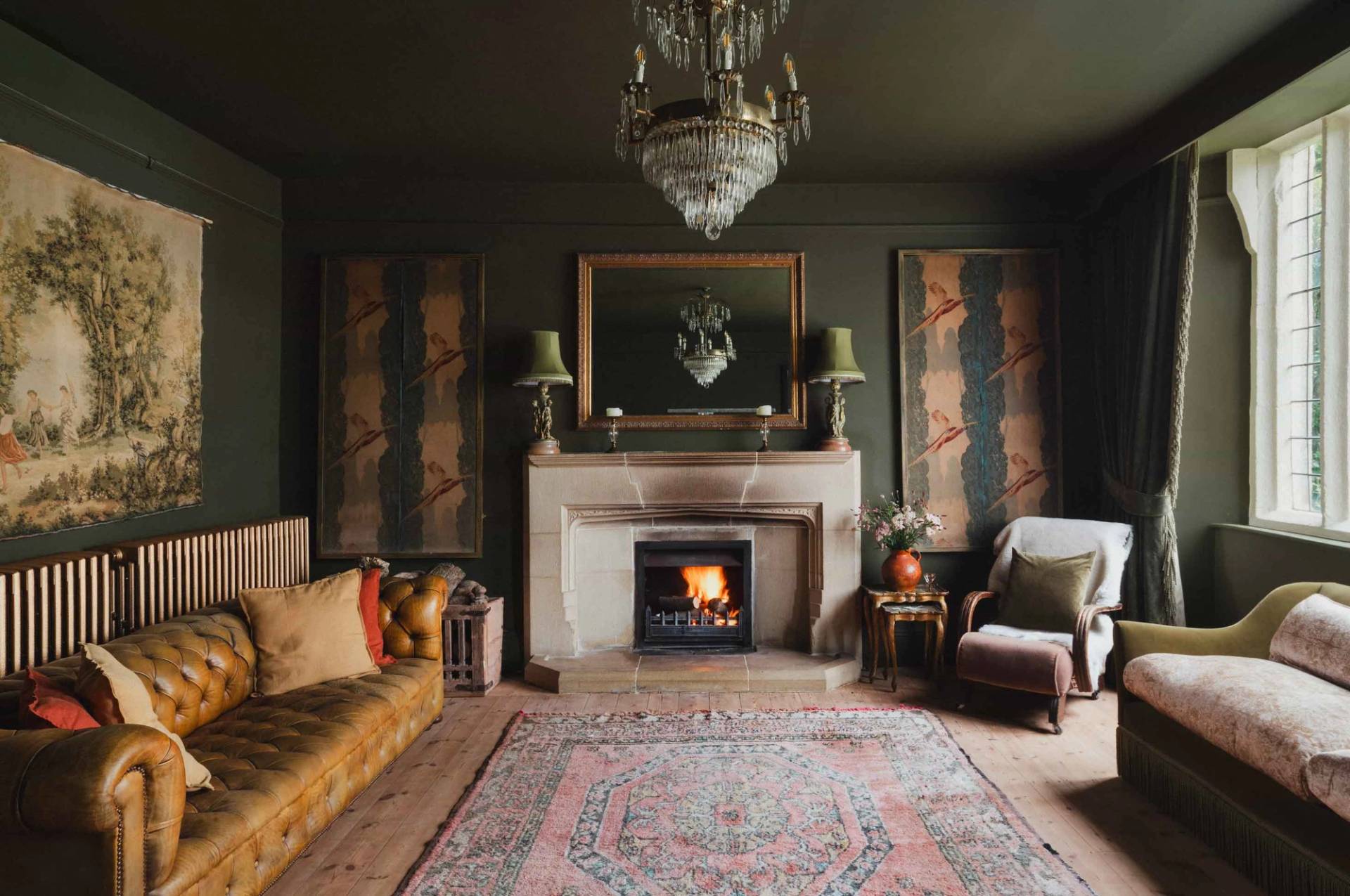 Moody green drawing room photoshoot location in a Cornish manor house from Love Locations, featuring an open stone fireplace hearth, traditional rug, and gold frame mirror.