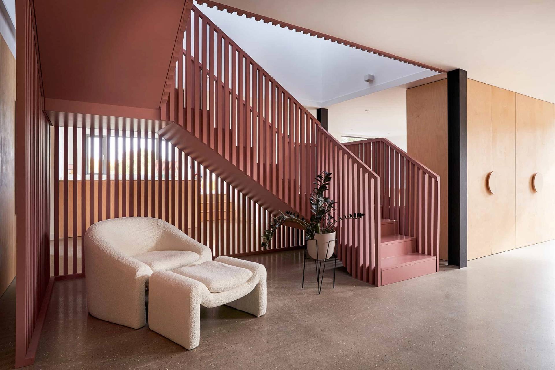 Bespoke terracotta pink slatted wooden staircase feature with cream bouclé armchair seating, Love Locations IP30.