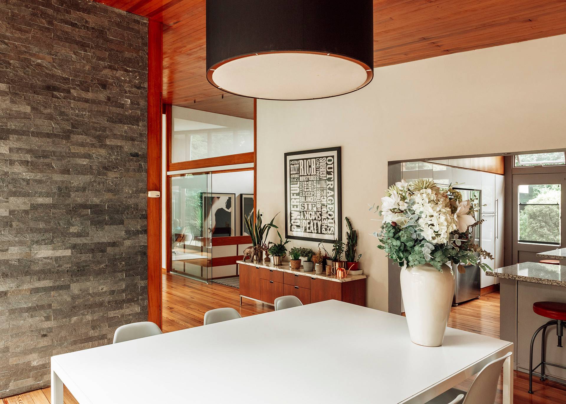 Minimalist white dining table setup illuminated by a large modern pendant light fixture inside a mid-century home, Love Locations BR1.