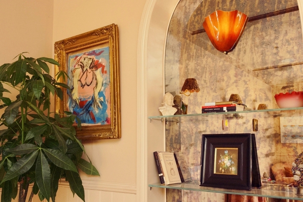 Detailed view of an arched shelving nook styled with framed art prints and books against patterned wallpaper, Love Locations.