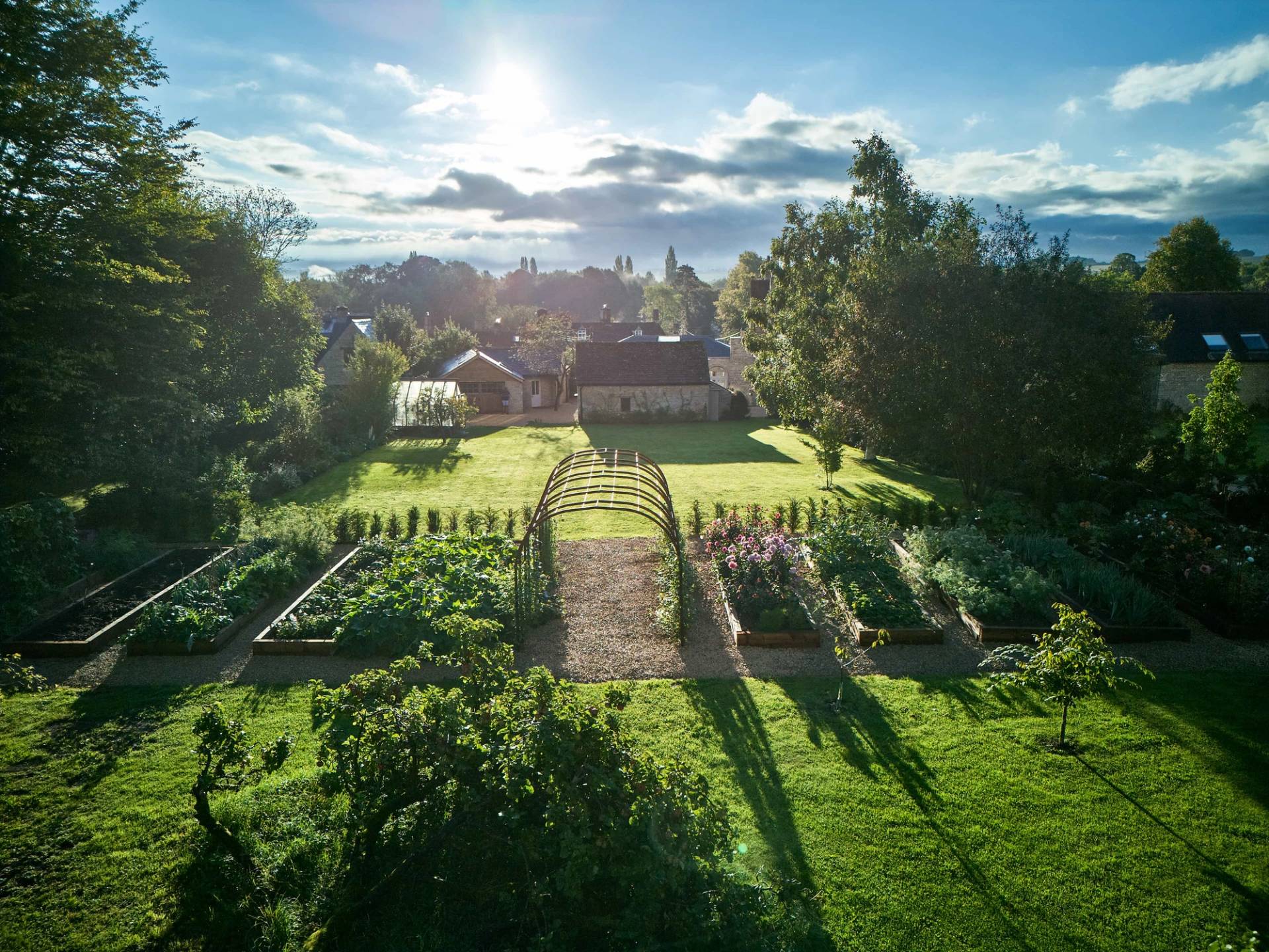 High-angle aerial drone view of a manicured kitchen garden, vegetable beds, and extensive Cotswold grounds, Love Locations.