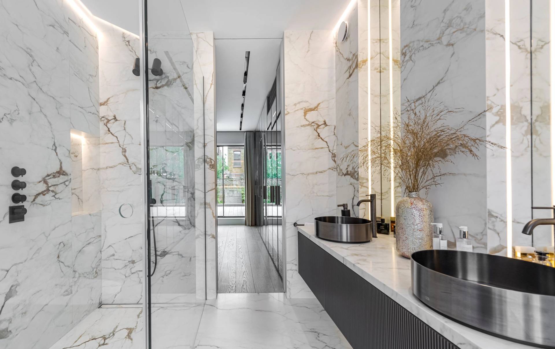 Double sink vanity unit with black countertop, gold spouts, and white veined marble wall tiles, Love Locations SW11.