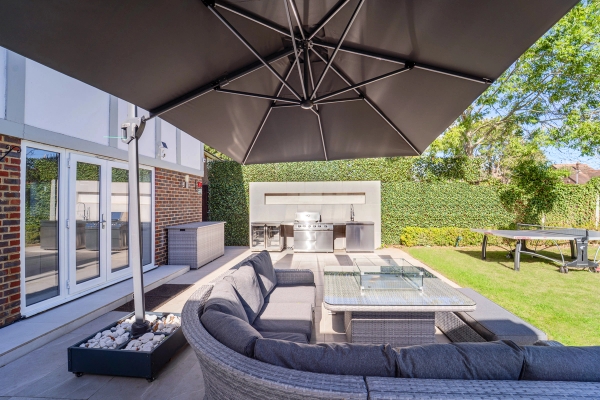 Outdoor lounge seating area set under a large black parasol beside an outdoor kitchen BBQ, Love Locations RM11.