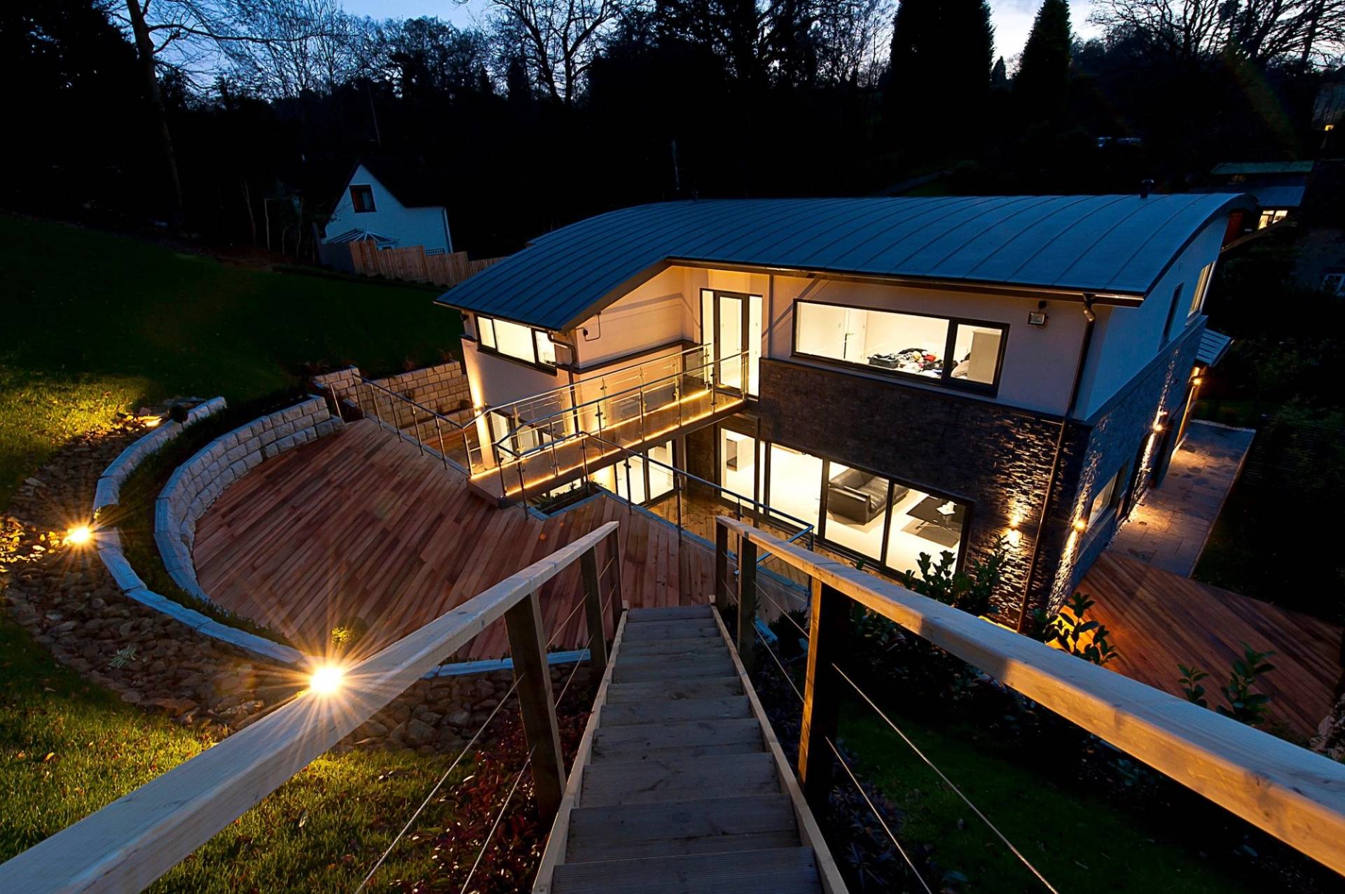 High-angle evening view looking down a lit wooden staircase onto a stunning architectural garden terrace assembly, Love Locations.