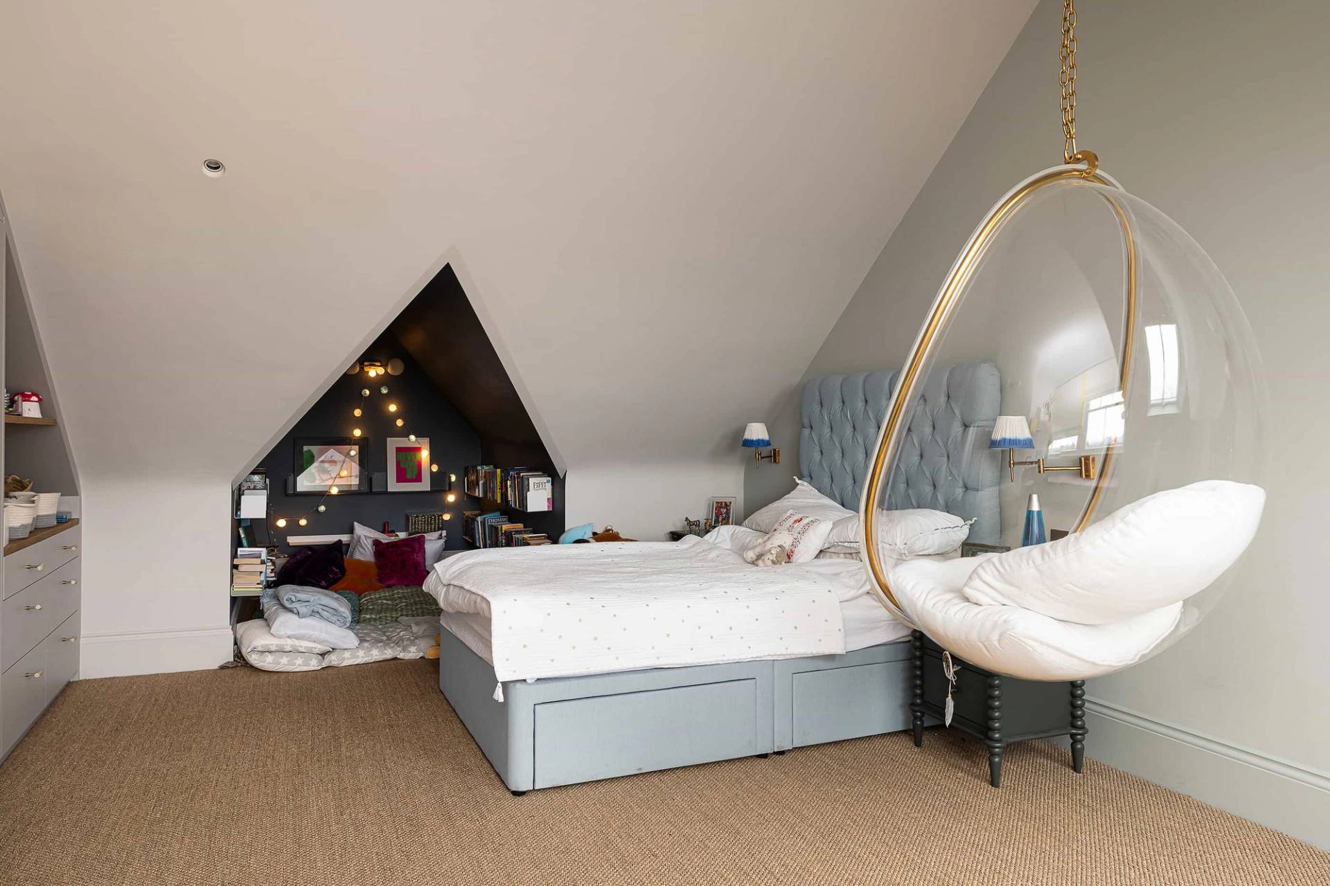 Attic bedroom suite featuring a light blue upholstered bed, sloped ceilings, and a hanging clear acrylic bubble chair, ideal for youth lifestyle brand filming, Love Locations NW6.