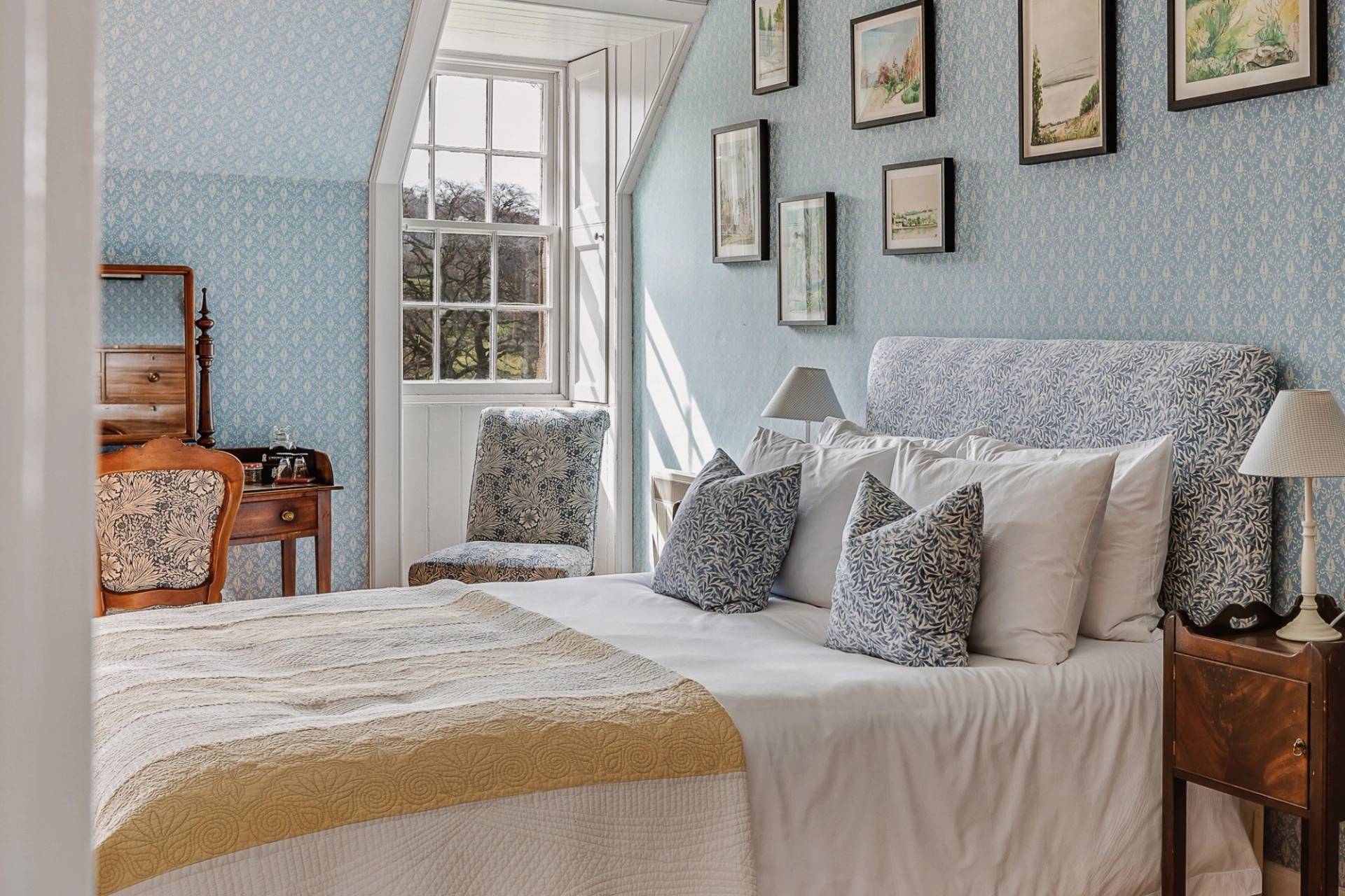 Sunlit bedroom featuring a grey upholstered headboard, light blue walls, and gallery picture frame wall, Love Locations KY15.