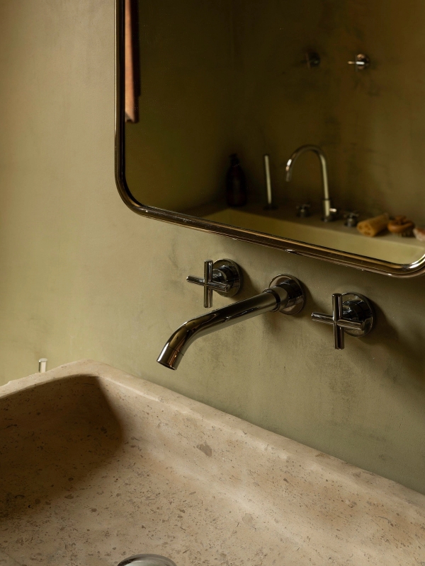 Close-up detail of a minimalist wall-mounted brass tap and microcement sink basin, Love Locations 2705-064.