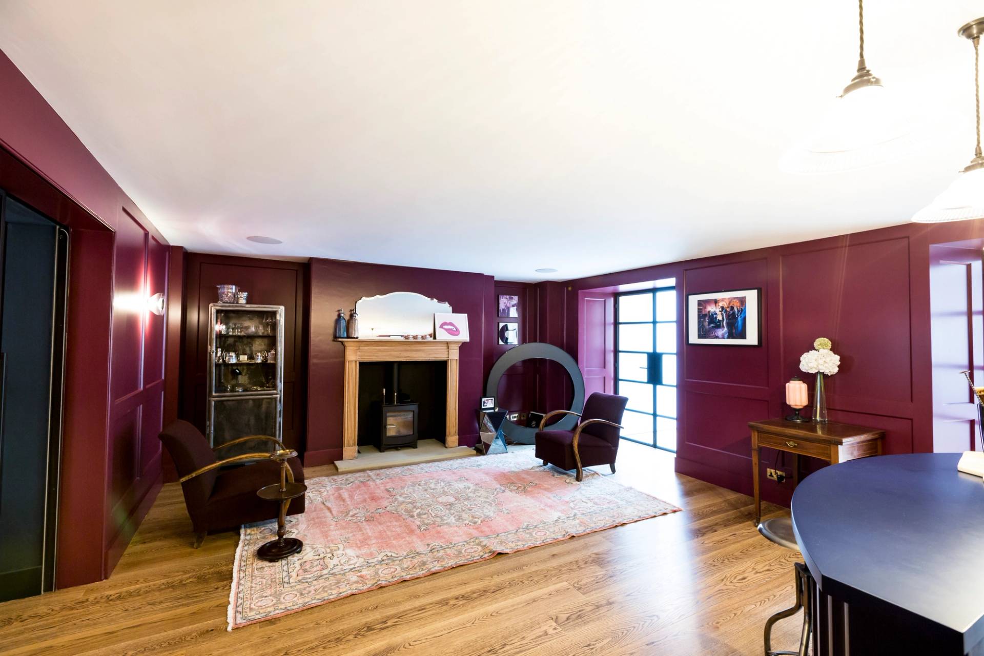 Plum painted entertainment room in Camberwell, SE5 with brick fireplace, log burner, and large oriental rug via Love Locations.