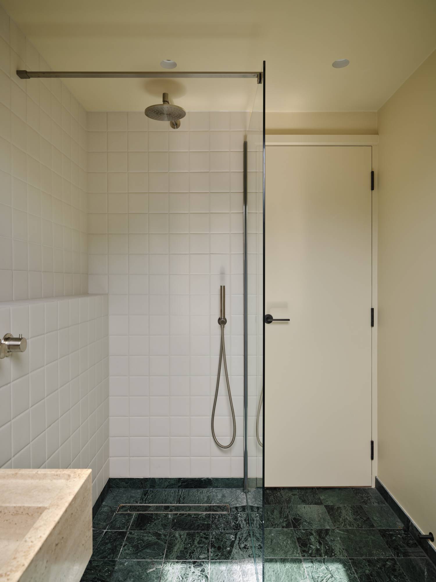 Love Locations modern wet room location SE23: Minimalist walk-in shower area lined with crisp white grid tiling and a glass panel partition screen, tailored for product placement.