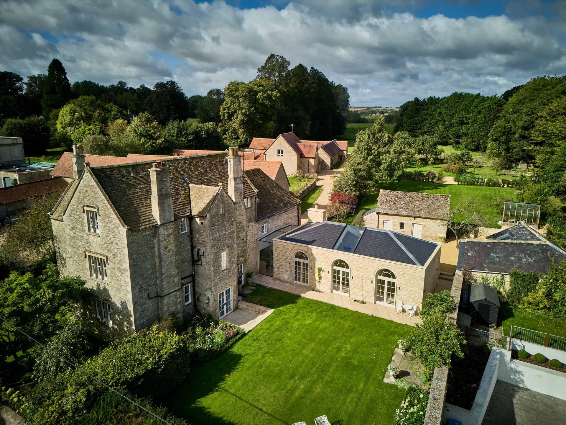 Aerial hero cover image of a historic Cotswold stone estate and modern vaulted extension in Shipton Under Wychwood, OX7 featuring pristine lawns and rural landscapes, the ultimate high-visibility backdrop for period film drama, luxury car commercials, and high-end brand campaigns via Love Locations.
