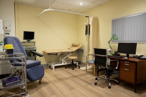 Examining room with medical couch, overhead lamp, and office desk setup, Love Locations UB4.