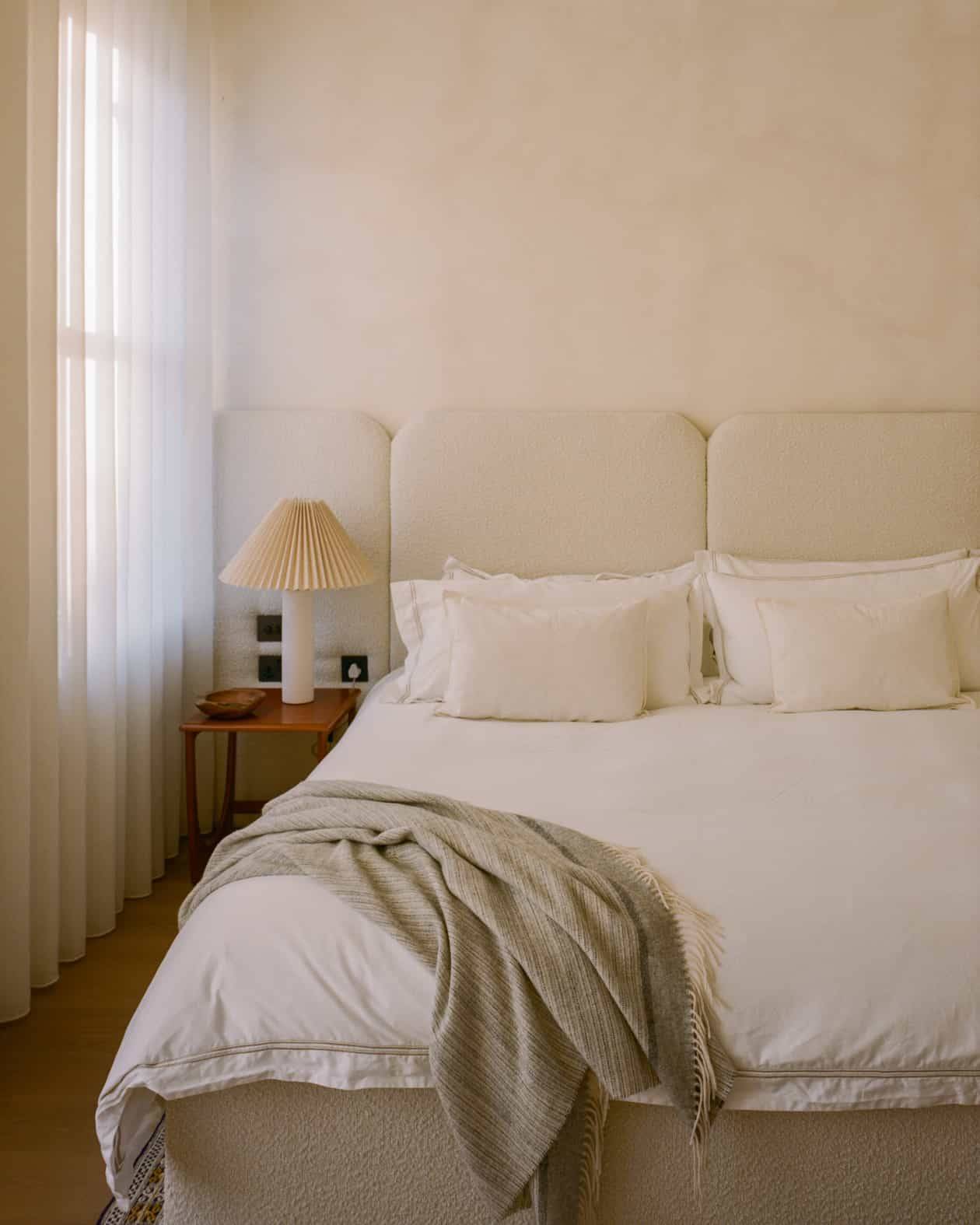 Minimalist master bedroom suite featuring textured plaster walls, cream upholstered headboard, and sheer curtains, Love Locations SW4.
