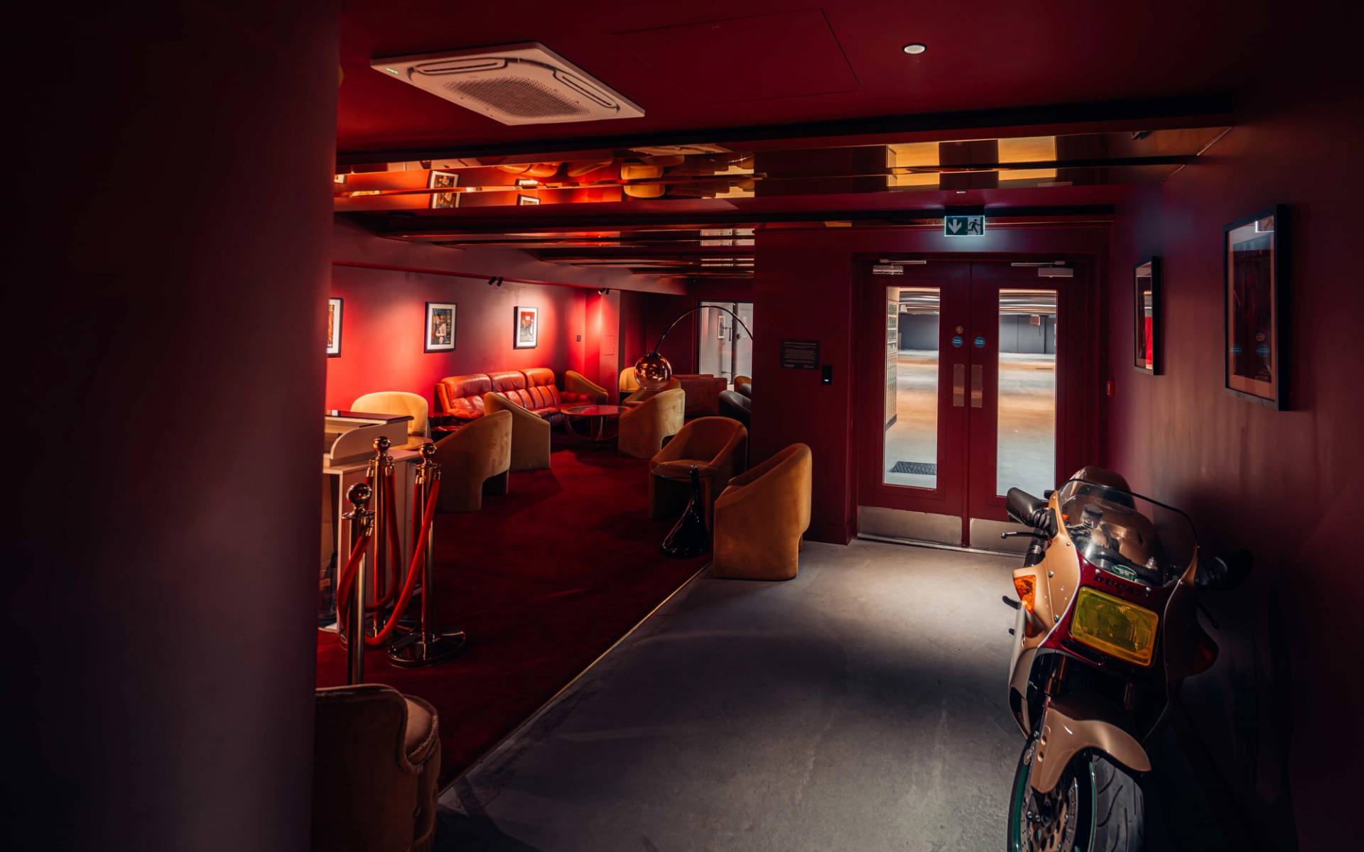 Moody red-lit lounge alcove with velvet armchairs and dark carpets in Brentford TW8 via Love Locations.
