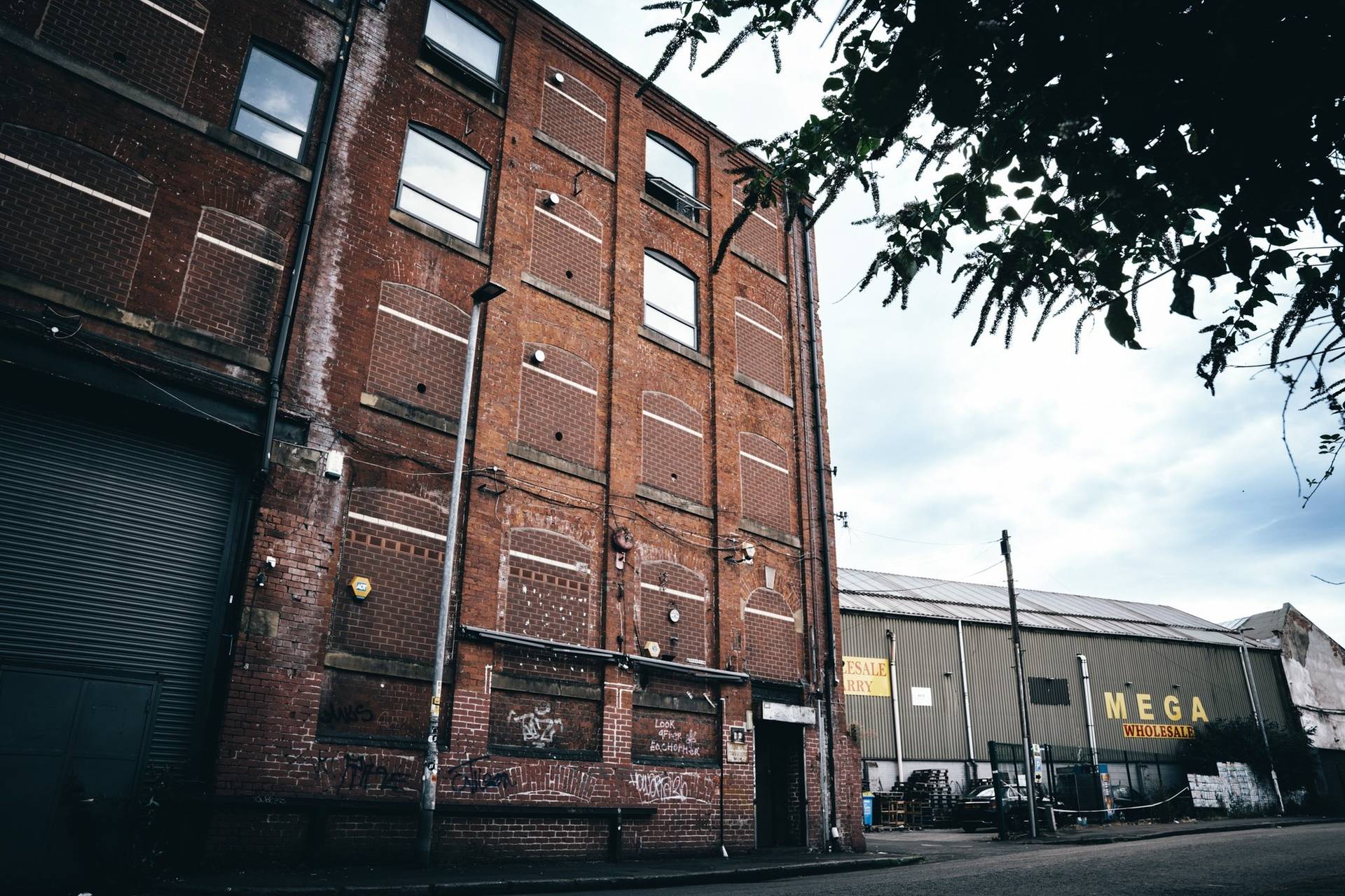 Tall historic multi-storey red brick warehouse facade in Cheetham Hill Manchester M3 by Love Locations.