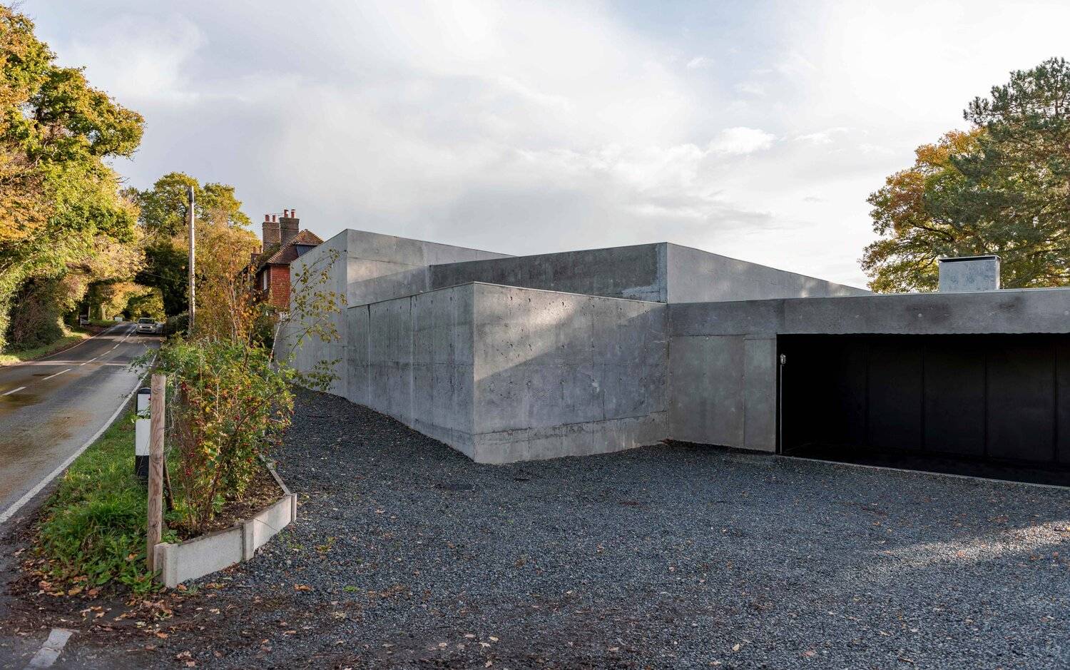 Architectural brutalist concrete home front entrance with gravel driveway and board-marked concrete walls, Love Locations BN7.