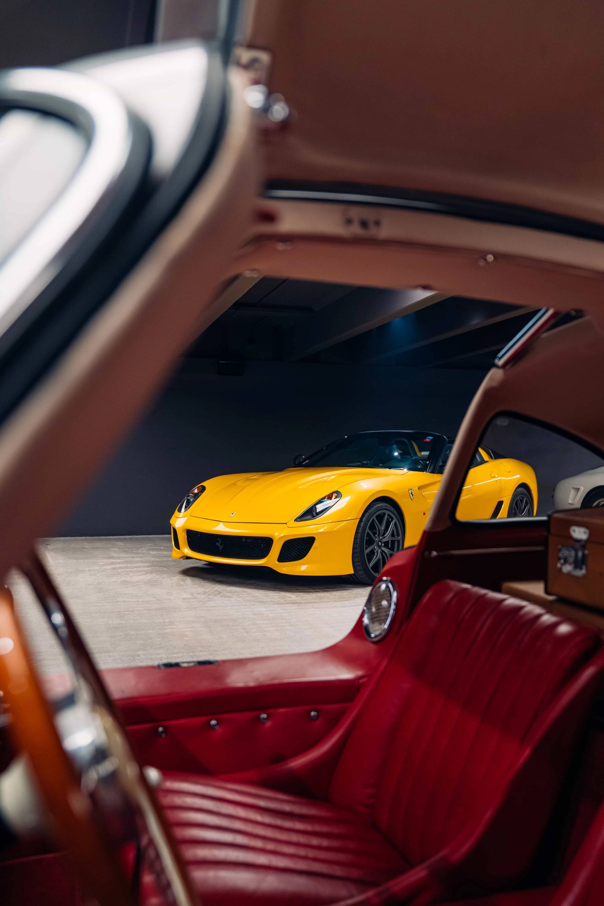 Interior view from inside a luxury vehicle looking toward a yellow sports car in an underground concrete shoot space via Love Locations.