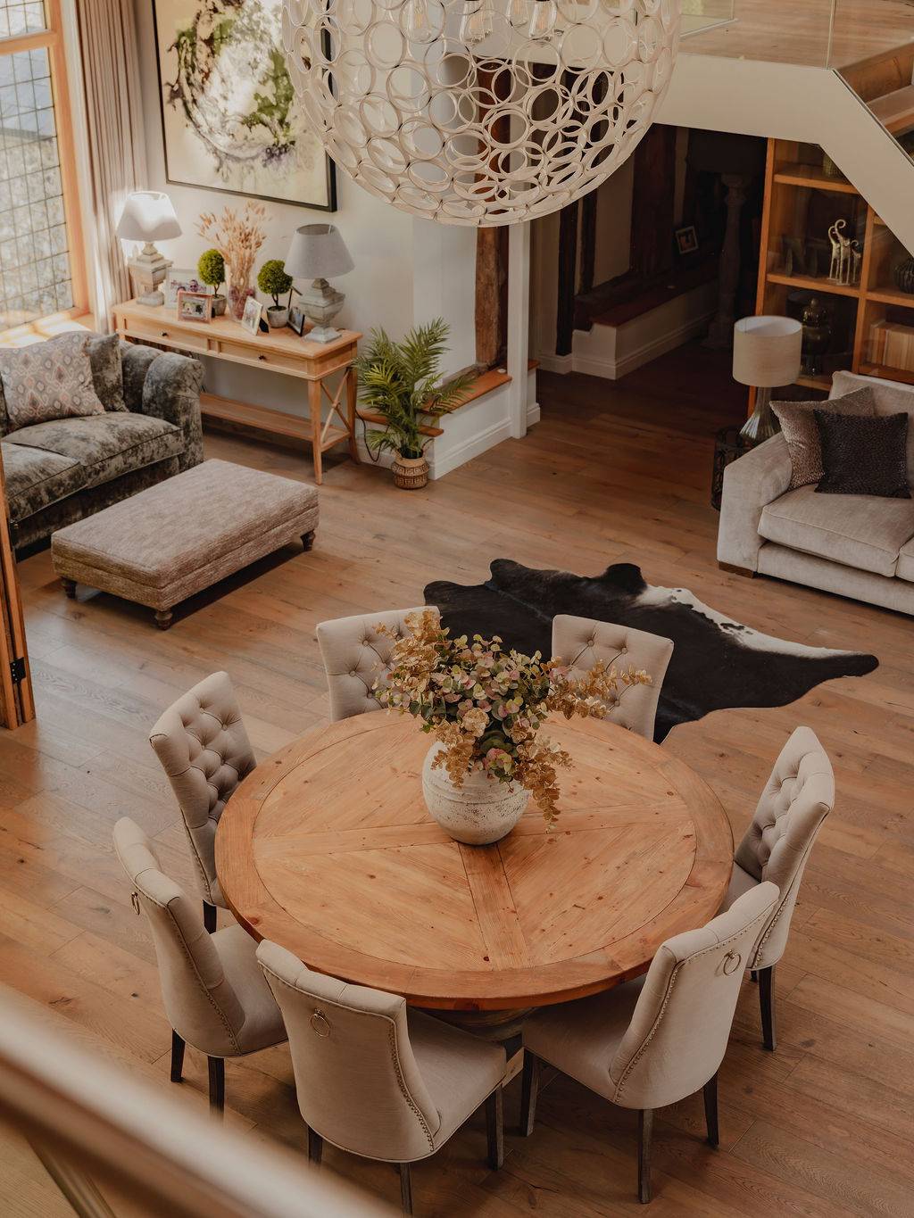 High-angle bird's-eye perspective of a round dining table setup and cowhide rug inside a grand barn hall, Love Locations