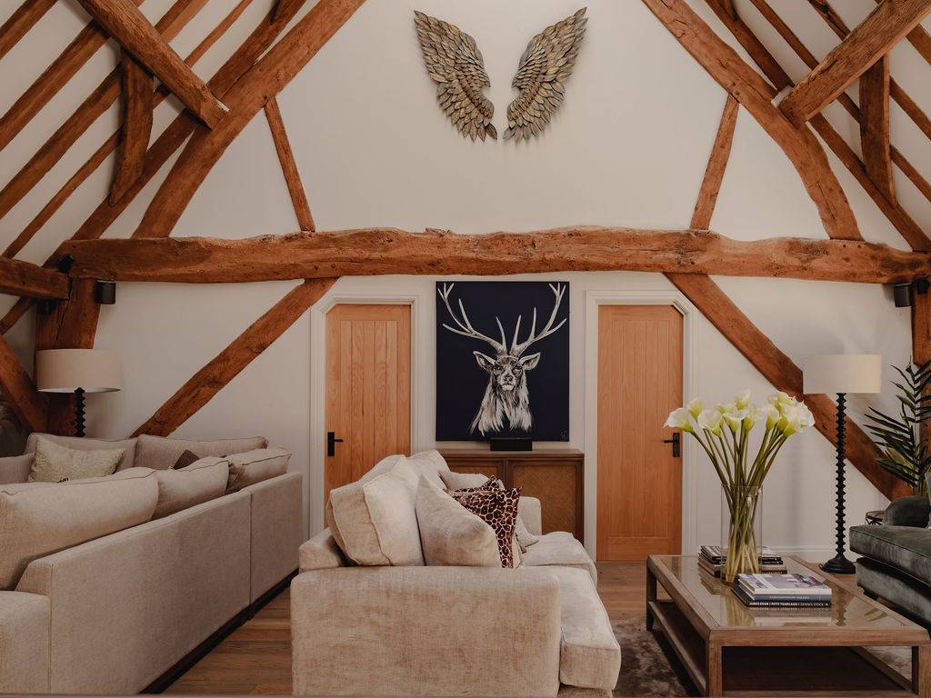 Mezzanine living room area with cream plush sofas set under vaulted timber rafters, Love Locations.