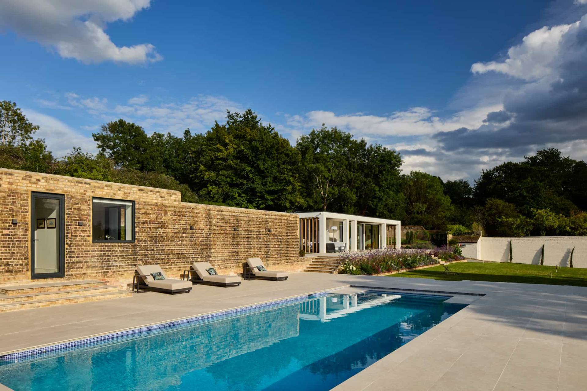 Luxury outdoor swimming pool area with sun loungers, yellow brick feature wall, and landscaped gardens, perfect for swimwear brand shoots, Love Locations.