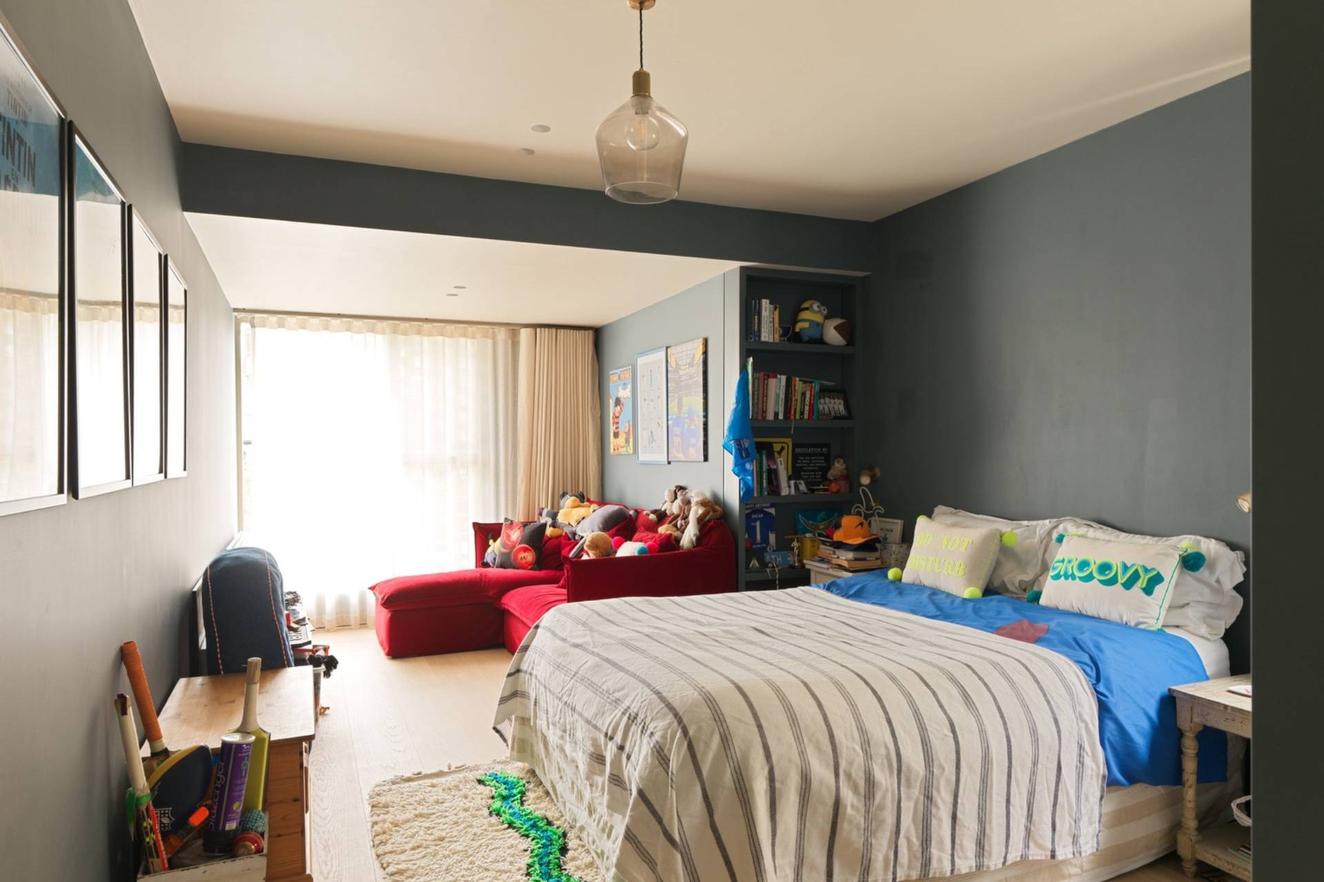 Spacious children's or teenager's bedroom film set featuring blue accent walls, bed with striped coverlet, and floor-to-ceiling glass doors via Love Locations.