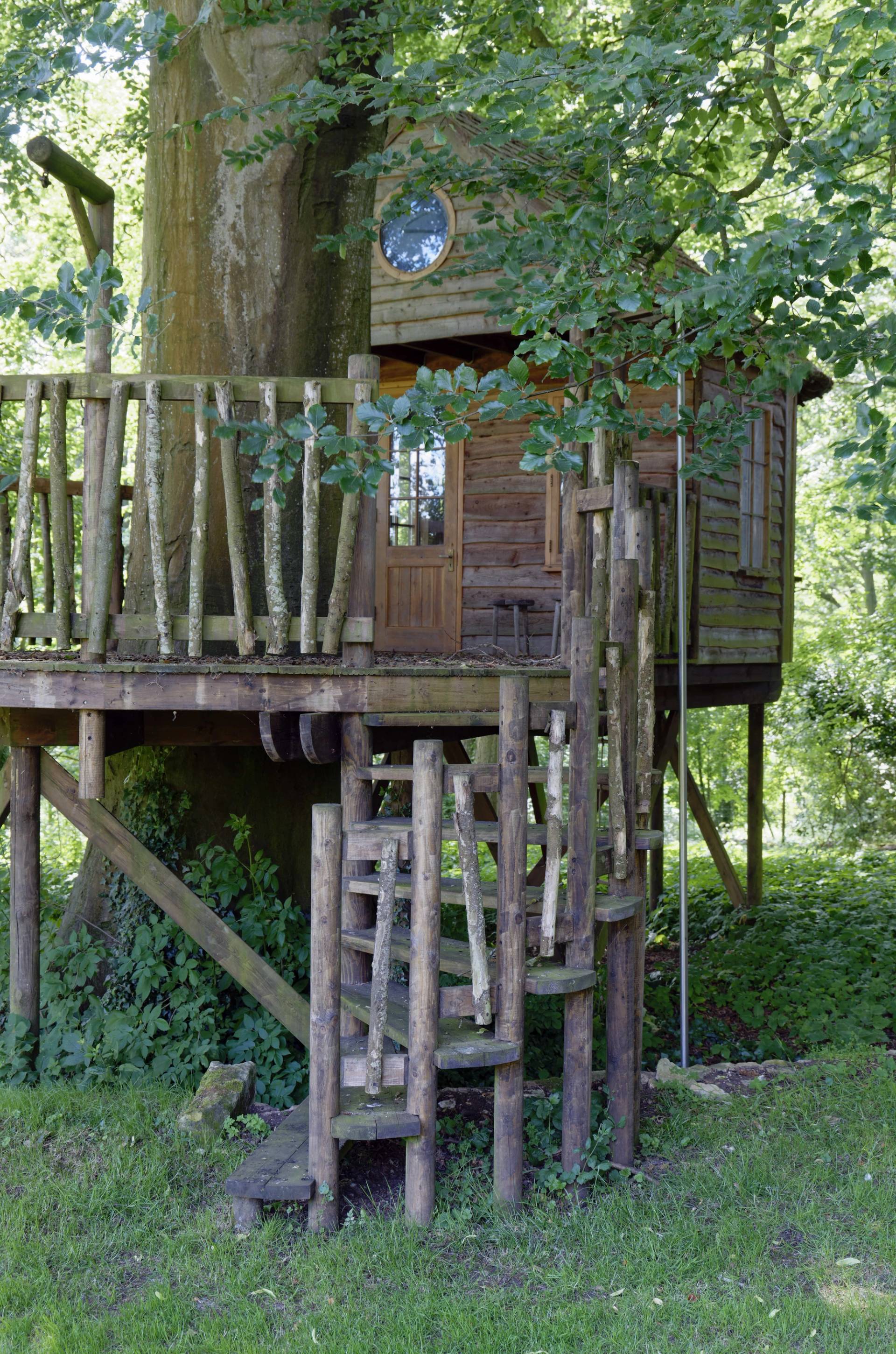 Rustic wooden treehouse structure set within mature woodland trees on private estate grounds, Love Locations OX7.