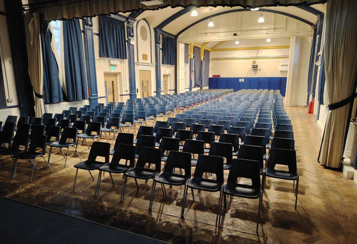 Grand school hall shoot space with arranged rows of black seating, arched architectural beams, and balcony view in Sittingbourne Kent ME10 via Love Locations.