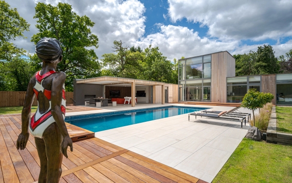 Love Locations ultra-modern house shoot location Godalming: Sunlit swimming pool wrapped in premium wooden decking and flat green lawns, optimized for swimwear campaigns and cinematic film.
